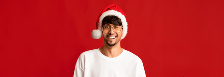 Smiling Man in Santa Hat Celebrating Holiday Season Against Red Backgroundの写真素材