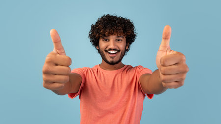 Smiling Young Eastern Man Gives Thumbs up Against Blue Background in Studio Setting