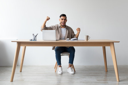 Excited Man Celebrates Success at Home Office With Laptop and Joyful Expressionの写真素材