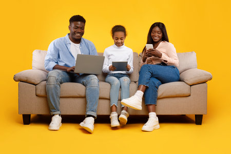 Happy Family of Three Enjoying Gadgets Together on a Cozy Sofa in a Bright Roomの写真素材