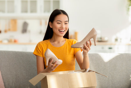 Happy Woman Unpacks High Heel Shoes From a Cardboard Box at Home in the Living Roomの写真素材