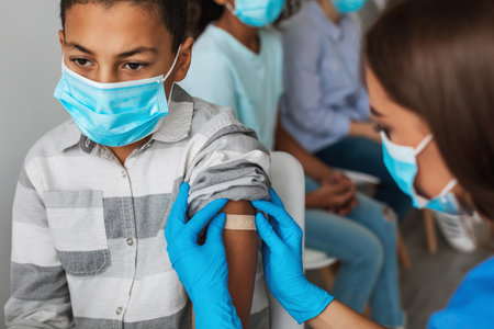 Nurse Administers Covid-19 Vaccine to Young Boy Indoors in Modern Clinic Settingの写真素材