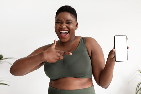 Joyful African American Plus Size Woman Shows Cellphone for Fitness App Recommendationの写真素材