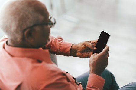 Senior Man Using Smartphone While Sitting Comfortably in a Modern Indoor Spaceの写真素材