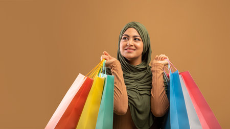 Happy Muslim Woman Enjoys Seasonal Sales While Carrying Colorful Shopping Bags in Modern Settingの写真素材