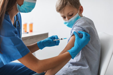 Nurse Administers Covid-19 Vaccine to Preteen Boy in Clinic Setting for Health Protectionの写真素材