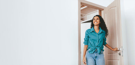 Joyful Woman Enters a Bright Room Through an Open Door With a Welcoming Smileの写真素材