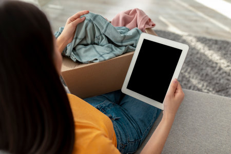 Young Woman Reviews Online Shopping Order While Relaxing at Home With New Clothesの写真素材