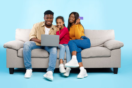Happy Black Family Enjoying Online Shopping Together on a Couch in a Bright Studio