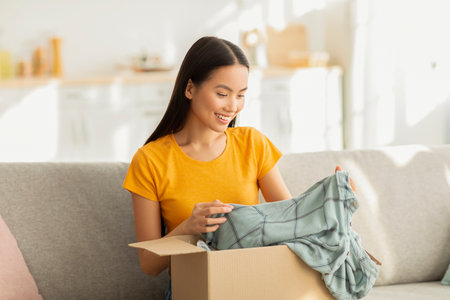 Satisfied Woman Unboxing Parcel of New Shirt While Relaxing on Sofa in Living Room
