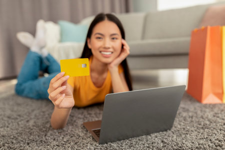 Positive Korean Woman Enjoys Online Shopping While Relaxing on a Carpet in Her Living Roomの写真素材