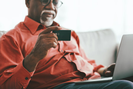 Older Man Using Contactless Card While Working on Laptop at Homeの写真素材