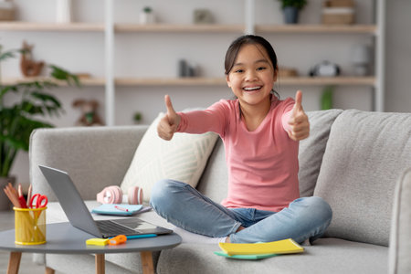Young Girl Expressing Happiness While Studying at Home on a Cozy Sofa With a Laptop and Colorful...
