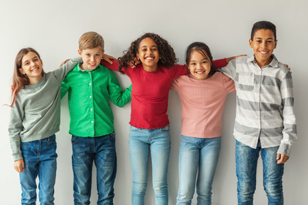 Cheerful Multiethnic Children Embrace Friendship and Joy While Posing Indoors Against a Gray Wallの写真素材