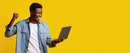 Man Celebrating Success While Using a Laptop Against a Bright Yellow Backgroundの写真素材