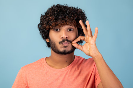 Millennial Man Keeps Secret With Zipped Lips Gesture Against Blue Backgroundの写真素材