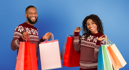 Bought a lot of purchases, seasonal sale concept. Happy african american spouses holding many colored shopping bagsの写真素材