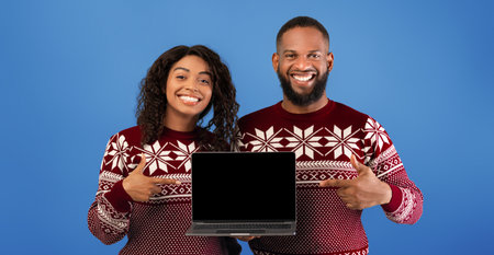 Christmas online shopping. Happy african american couple showing laptop with empty screen, pointing...