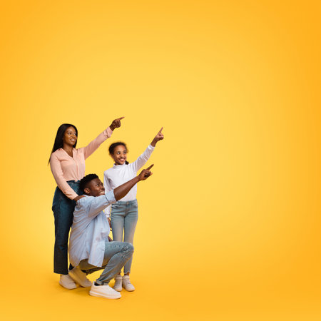 Happy African American Family of Three Posing and Pointing at Free Space in Bright Studio Settingの写真素材