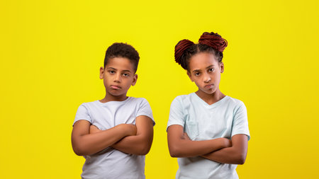 Two Children Pose With Serious Expressions Against a Bright Yellow Backgroundの写真素材