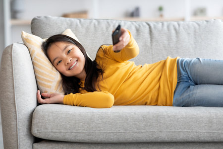 Young Girl Relaxing on Couch While Watching Television and Enjoying Her Time at Homeの写真素材