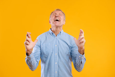 Hopeful Mature Man Crossing Fingers While Wishing for Good Luck in Studio Settingの写真素材