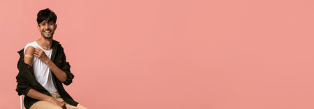 Young Man Sitting on Chair Against Pink Background Smiling and Enjoying the Momentの写真素材