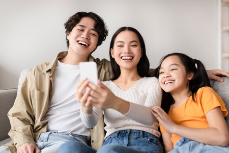 Three Friends Enjoy a Fun Moment Together While Smiling and Taking a Selfie at Home in Warm Afternoon Lightの写真素材