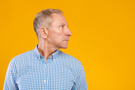 Mature Man Posing in Serious Profile Against Vibrant Yellow Studio Backgroundの写真素材