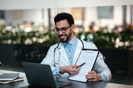 Doctor Explaining Patient Information While Working on a Laptop in a Modern Medical Officeの写真素材