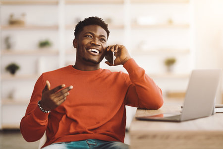 Smiling Man Engaging in a Phone Conversation at a Cozy Workspace in the Morningの写真素材