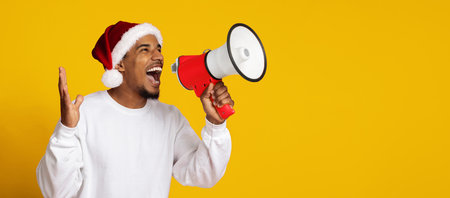 Man in Santa Hat Enthusiastically Using Megaphone Against Yellow Backgroundの写真素材
