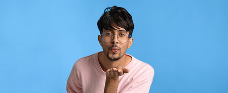 Young Man Blowing a Kiss Against a Blue Background in a Playful Moment