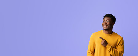 Smiling Man in Yellow Sweater Pointing to the Side Against a Purple Backgroundの写真素材