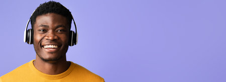 Young Man Enjoying Music With Headphones on a Purple Background While Smiling Brightlyの写真素材