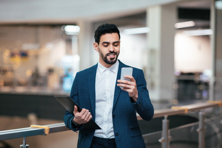 Business Professional Checks Smartphone While Standing in Modern Office Environment During Daytime