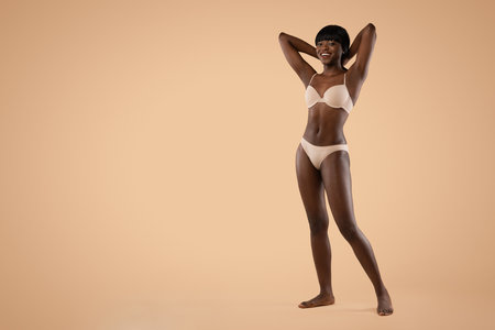 Happy Black Lady Poses Confidently in Underwear Against Beige Backgroundの写真素材