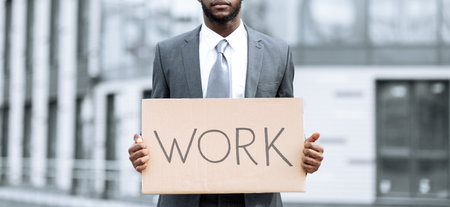 Individual in Business Attire Holds Sign With Work Message in Urban Setting During Daytimeの写真素材