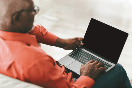 Elderly Man Using Laptop While Sitting on a Comfortable Couch Indoorsの写真素材