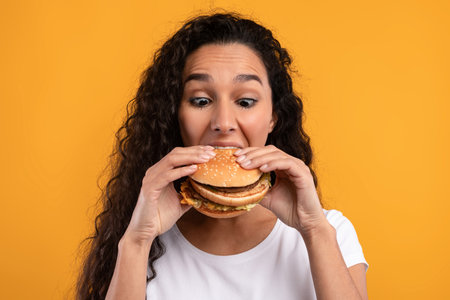 Funny Latin Lady Enjoying a Big Burger in a Vibrant Studio Settingの写真素材