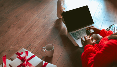 Person Working on Laptop With Gifts and Coffee on the Floor in Cozy Setting