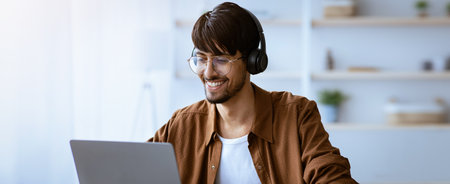 Young Man Smiles While Working on Laptop in Modern Home Office During Daytime