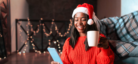 Smiling Woman in Festive Sweater Enjoying a Warm Drink While Looking at a Tablet Indoors
