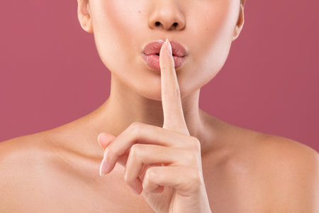 Cropped View of a Woman Making a Silence Gesture Against a Purple Backdrop in a Studioの写真素材