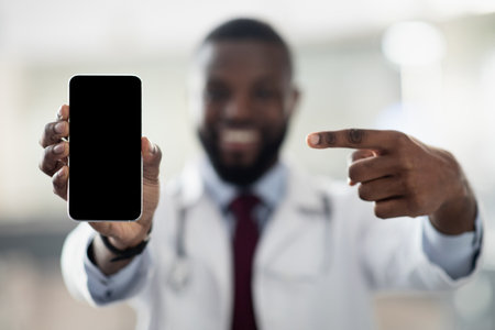 Cheerful african american doctor pointing at smartphone, mockupの写真素材