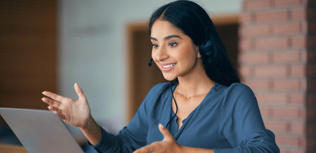 Young Woman Engages in a Virtual Meeting While Using a Headset and Laptopの写真素材
