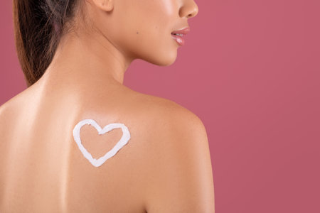 Pretty Korean Lady Applies Body Lotion With Heart Shape Design on Back in Purple Studioの写真素材