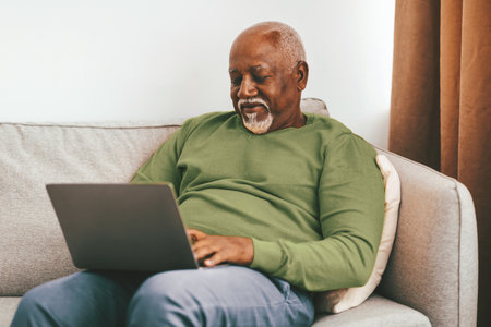 Senior Man Using Laptop on a Sofa in His Living Room During Daytimeの写真素材