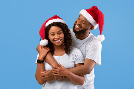 Loving african american couple in Santa hats hugging on yellow studio background, celebrating New Year or Christmasの写真素材