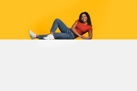 Young Woman Relaxing in Casual Outfit Against Bright Yellow Backdropの写真素材